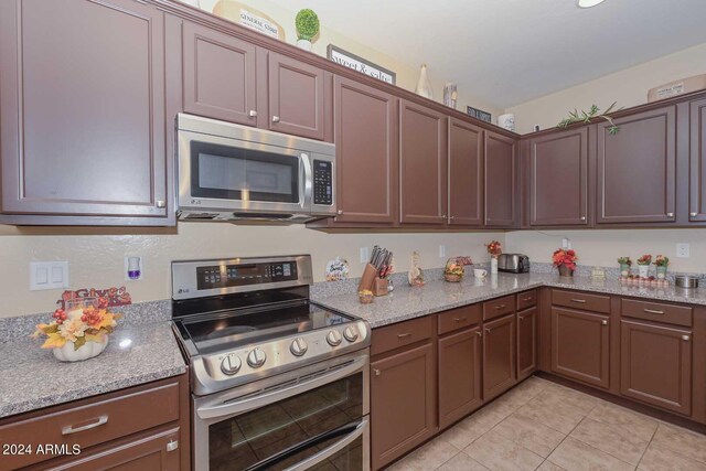 kitchen with stainless steel appliances, light stone counters, and light tile patterned floors