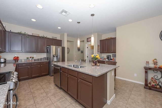 kitchen with an island with sink, light stone countertops, stainless steel appliances, decorative light fixtures, and sink