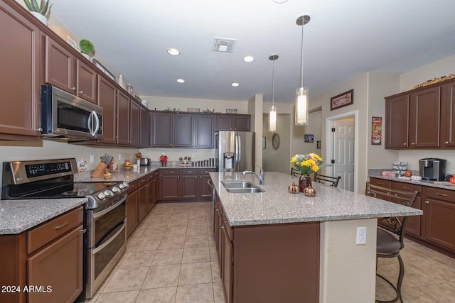 kitchen with light stone counters, sink, a kitchen bar, stainless steel appliances, and a center island with sink