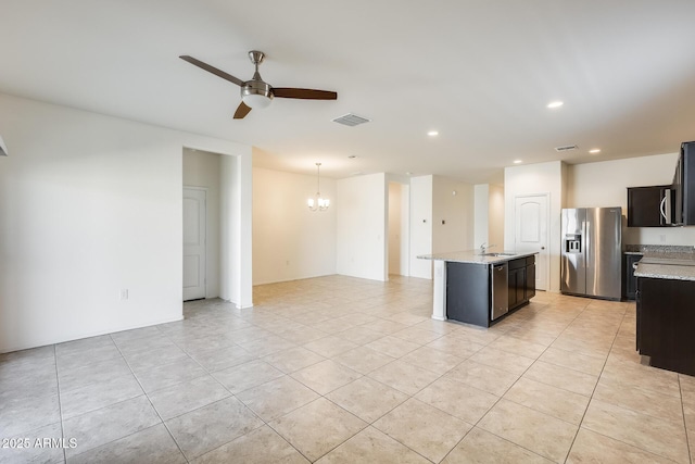 kitchen featuring light stone counters, ceiling fan with notable chandelier, stainless steel appliances, visible vents, and a center island with sink