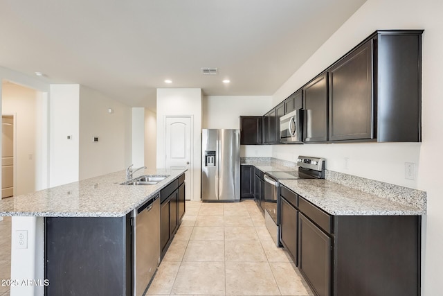 kitchen featuring stainless steel appliances, a sink, a center island with sink, and light stone countertops