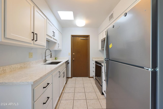 kitchen featuring appliances with stainless steel finishes, a skylight, sink, light tile patterned floors, and white cabinetry