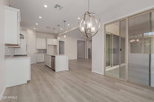 kitchen featuring stainless steel dishwasher, a chandelier, decorative light fixtures, a center island with sink, and white cabinetry