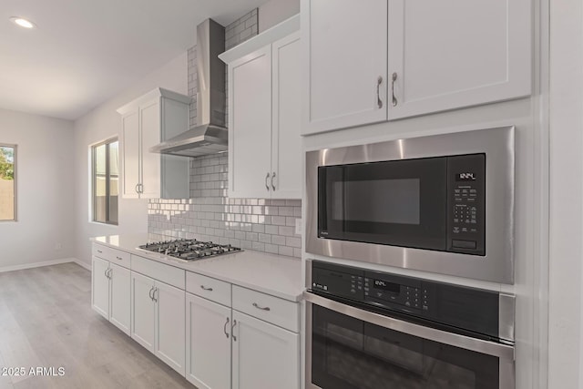 kitchen with white cabinetry, wall chimney exhaust hood, light hardwood / wood-style floors, decorative backsplash, and appliances with stainless steel finishes