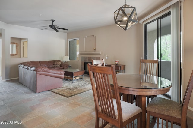 dining space with a tile fireplace, a ceiling fan, baseboards, and light stone finish floors