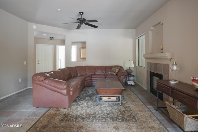 living area with a ceiling fan, a tile fireplace, and baseboards