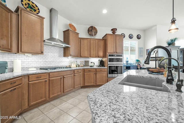 kitchen with stainless steel appliances, sink, wall chimney range hood, and light stone counters