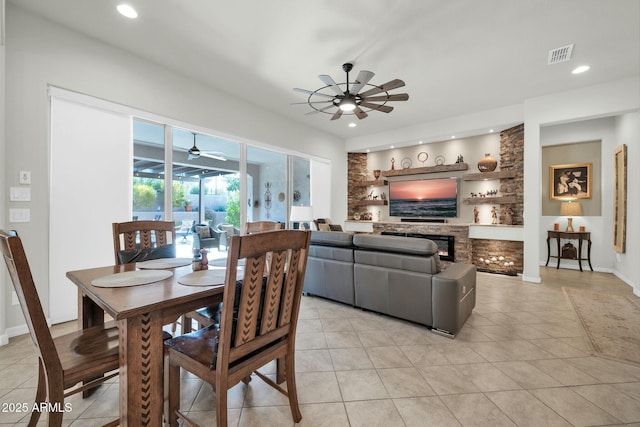 tiled dining room featuring ceiling fan and a stone fireplace