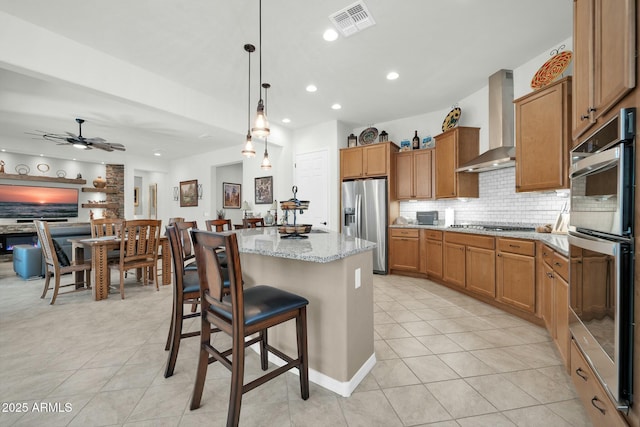 kitchen featuring a kitchen breakfast bar, a kitchen island, pendant lighting, stainless steel appliances, and wall chimney range hood