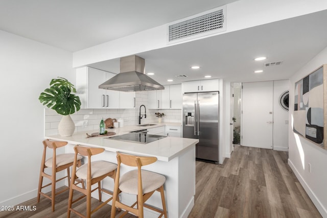 kitchen featuring stainless steel built in fridge, white cabinetry, light hardwood / wood-style floors, kitchen peninsula, and island range hood