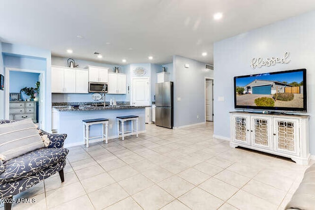 kitchen featuring light tile patterned floors, a breakfast bar, appliances with stainless steel finishes, dark stone countertops, and white cabinets