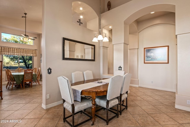 tiled dining area featuring a high ceiling and ceiling fan with notable chandelier