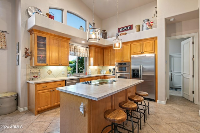 kitchen with appliances with stainless steel finishes, a towering ceiling, tasteful backsplash, sink, and a center island