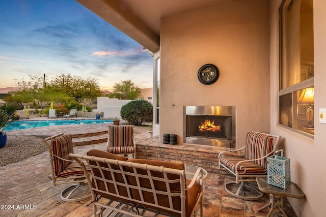 patio terrace at dusk featuring a fenced in pool and an outdoor fireplace