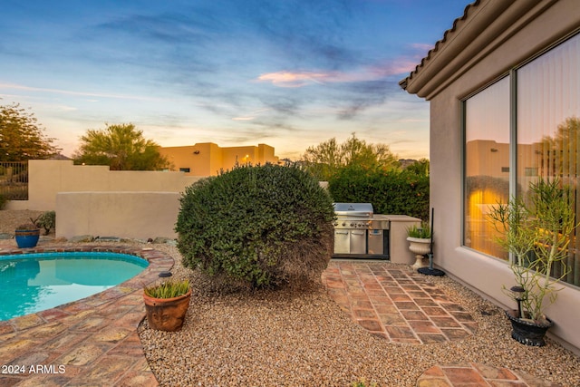 pool at dusk featuring an outdoor kitchen, a patio, and a grill