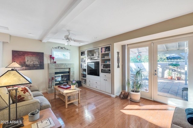 living room featuring french doors, hardwood / wood-style floors, ceiling fan, a premium fireplace, and beam ceiling