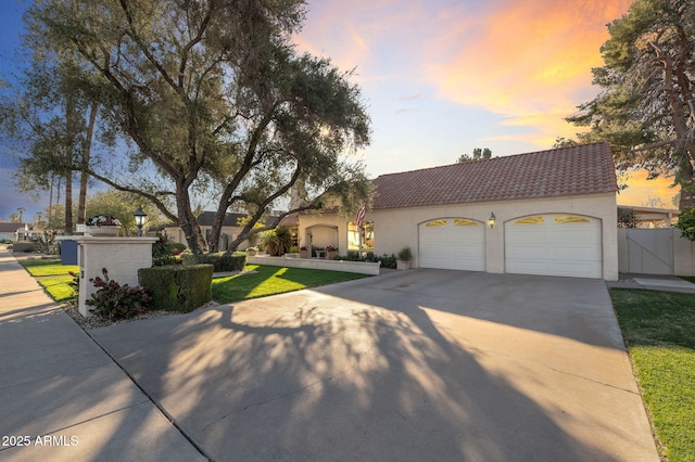 mediterranean / spanish home featuring concrete driveway, a tile roof, an attached garage, a gate, and a front yard