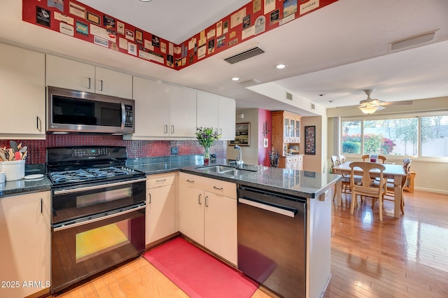 kitchen with black appliances, light wood-type flooring, kitchen peninsula, ceiling fan, and sink