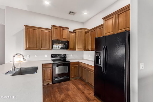 kitchen featuring brown cabinetry, dark wood finished floors, a sink, light countertops, and black appliances