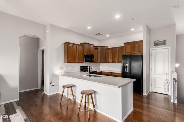 kitchen with a peninsula, dark wood-type flooring, arched walkways, a sink, and black appliances