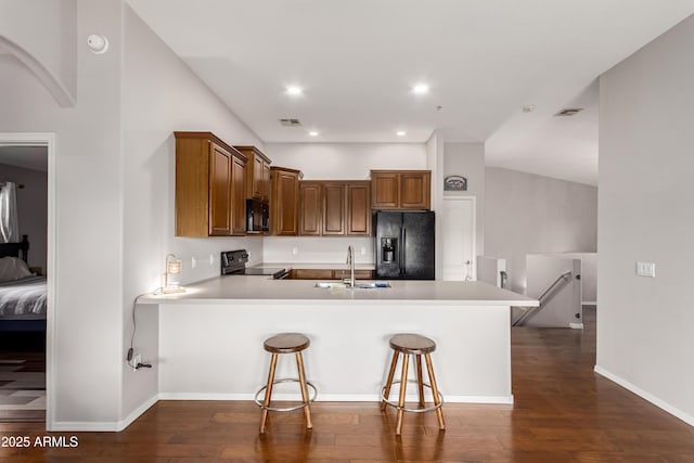 kitchen with a sink, dark wood-style flooring, black appliances, and a peninsula