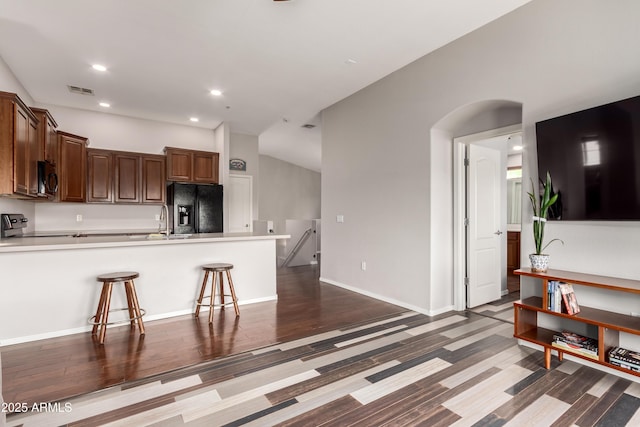kitchen with a peninsula, black refrigerator with ice dispenser, a breakfast bar, light countertops, and a sink