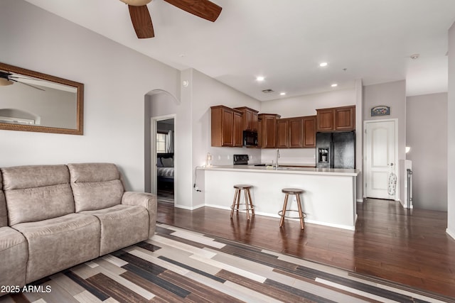 living area featuring visible vents, arched walkways, dark wood finished floors, and ceiling fan