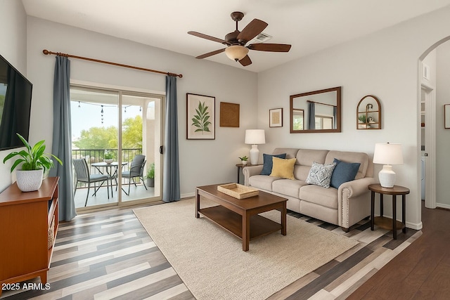 living room featuring baseboards, arched walkways, a ceiling fan, and wood finished floors
