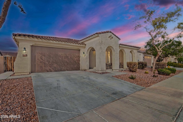 mediterranean / spanish house with stucco siding, a garage, a tiled roof, and concrete driveway