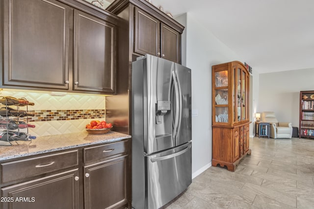 kitchen featuring light stone counters, baseboards, stainless steel fridge with ice dispenser, dark brown cabinets, and tasteful backsplash