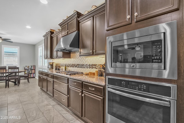 kitchen with backsplash, ceiling fan, under cabinet range hood, light stone counters, and stainless steel appliances