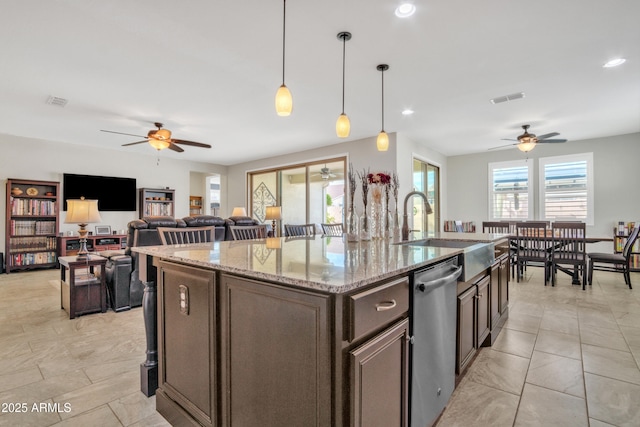 kitchen featuring visible vents, a kitchen island with sink, a sink, light stone counters, and dishwasher