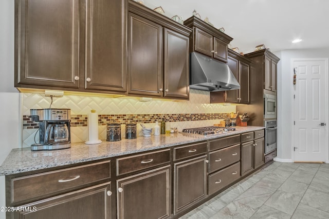 kitchen with marble finish floor, under cabinet range hood, stainless steel appliances, light stone countertops, and dark brown cabinets