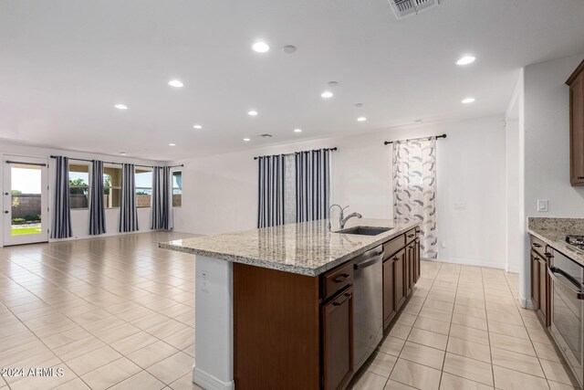 kitchen with dishwasher, an island with sink, sink, light stone countertops, and light tile patterned flooring