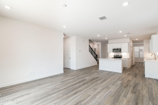 kitchen with sink, a center island, light hardwood / wood-style flooring, appliances with stainless steel finishes, and white cabinets