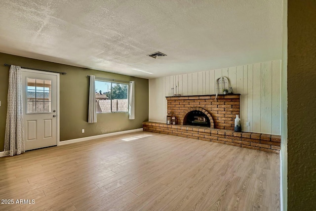 unfurnished living room with visible vents, a textured ceiling, light wood-style floors, baseboards, and a brick fireplace