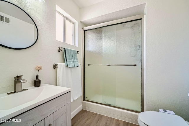 bathroom featuring visible vents, toilet, wood finished floors, and a stall shower