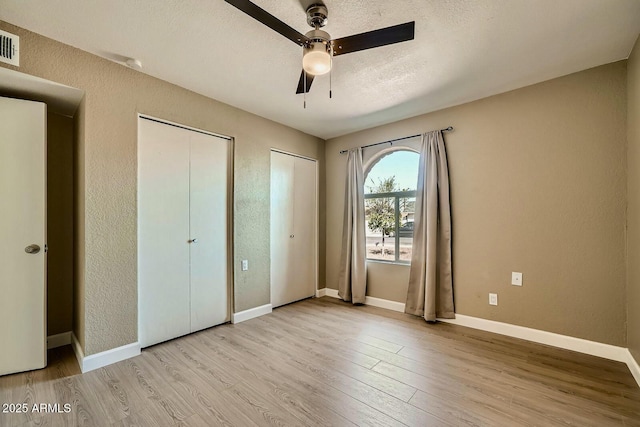 unfurnished bedroom featuring visible vents, two closets, a textured ceiling, wood finished floors, and a textured wall