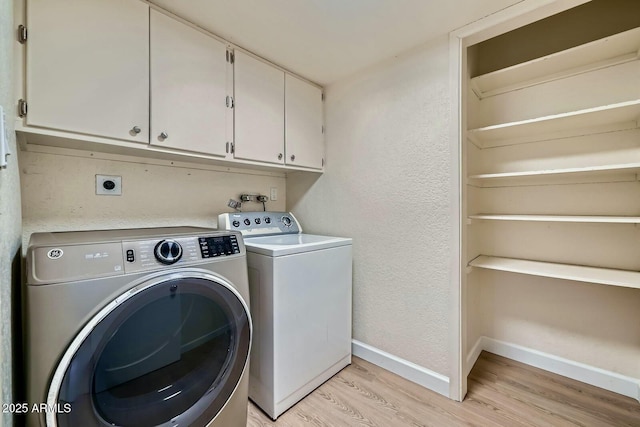 laundry area with baseboards, cabinet space, light wood-style floors, a textured wall, and washer and clothes dryer