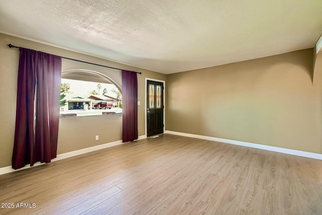 spare room featuring a textured ceiling, baseboards, and wood finished floors