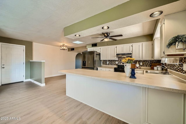 kitchen with a peninsula, a sink, stainless steel appliances, light countertops, and under cabinet range hood