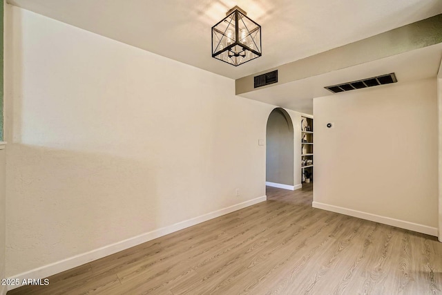 empty room with light wood-style floors, arched walkways, visible vents, and baseboards