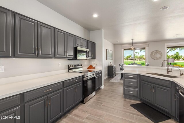 kitchen with light hardwood / wood-style flooring, stainless steel appliances, sink, and hanging light fixtures