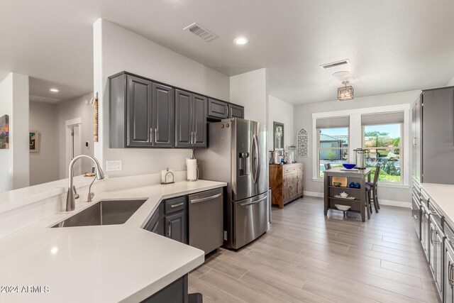 kitchen with appliances with stainless steel finishes, light hardwood / wood-style floors, kitchen peninsula, and sink