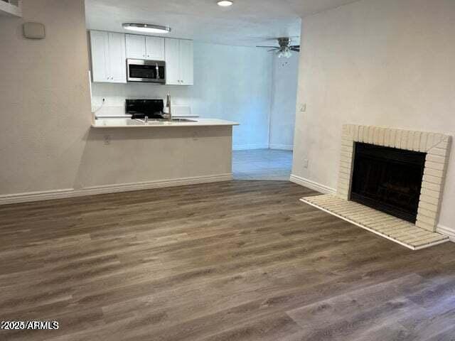 unfurnished living room with a fireplace, dark hardwood / wood-style flooring, ceiling fan, and sink