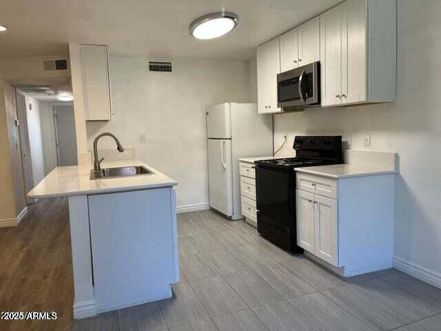 kitchen featuring white fridge, white cabinetry, black / electric stove, and sink