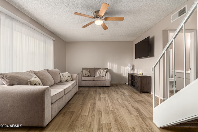 living room featuring ceiling fan, a textured ceiling, and light wood-type flooring