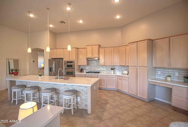 kitchen featuring appliances with stainless steel finishes, an island with sink, hanging light fixtures, and light brown cabinets