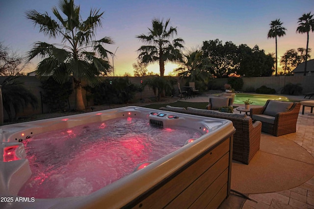 pool at dusk with a patio area and a hot tub