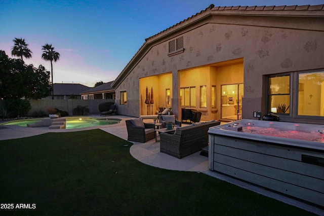 back house at dusk with a patio, outdoor lounge area, a pool with hot tub, and a lawn